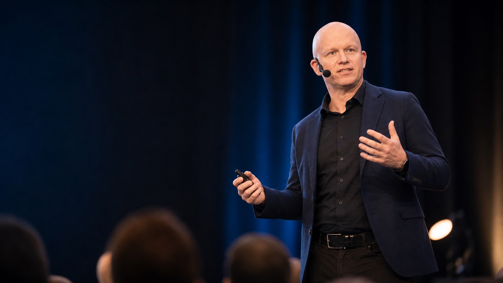 Janne Ikola speaking on stage with a headset microphone